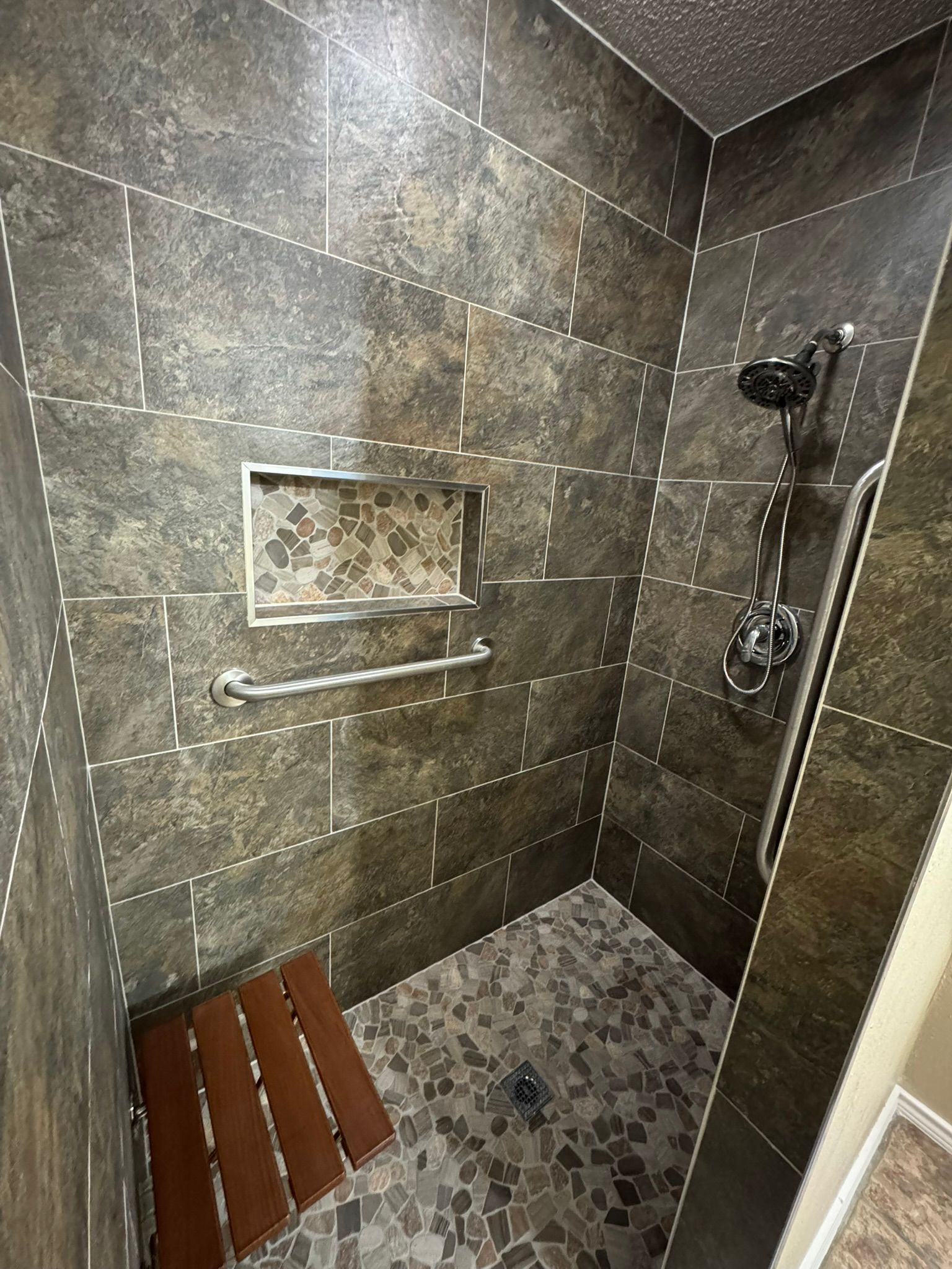 A bathroom with a walk in shower and a wooden bench.