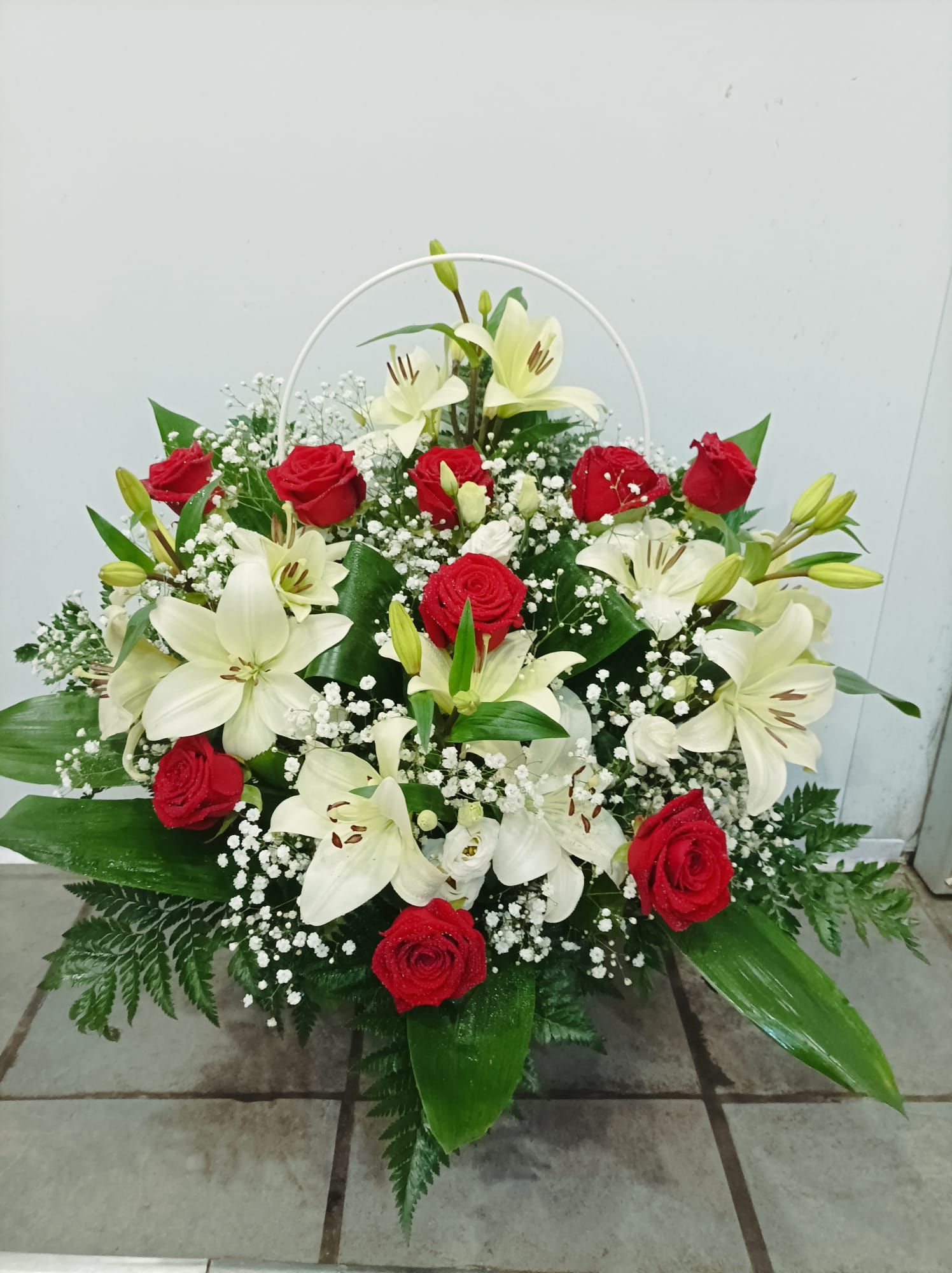 Composizione floreale: rose rosse, gigli bianchi e gypsophila, con verde, in un contenitore bianco poco profondo.