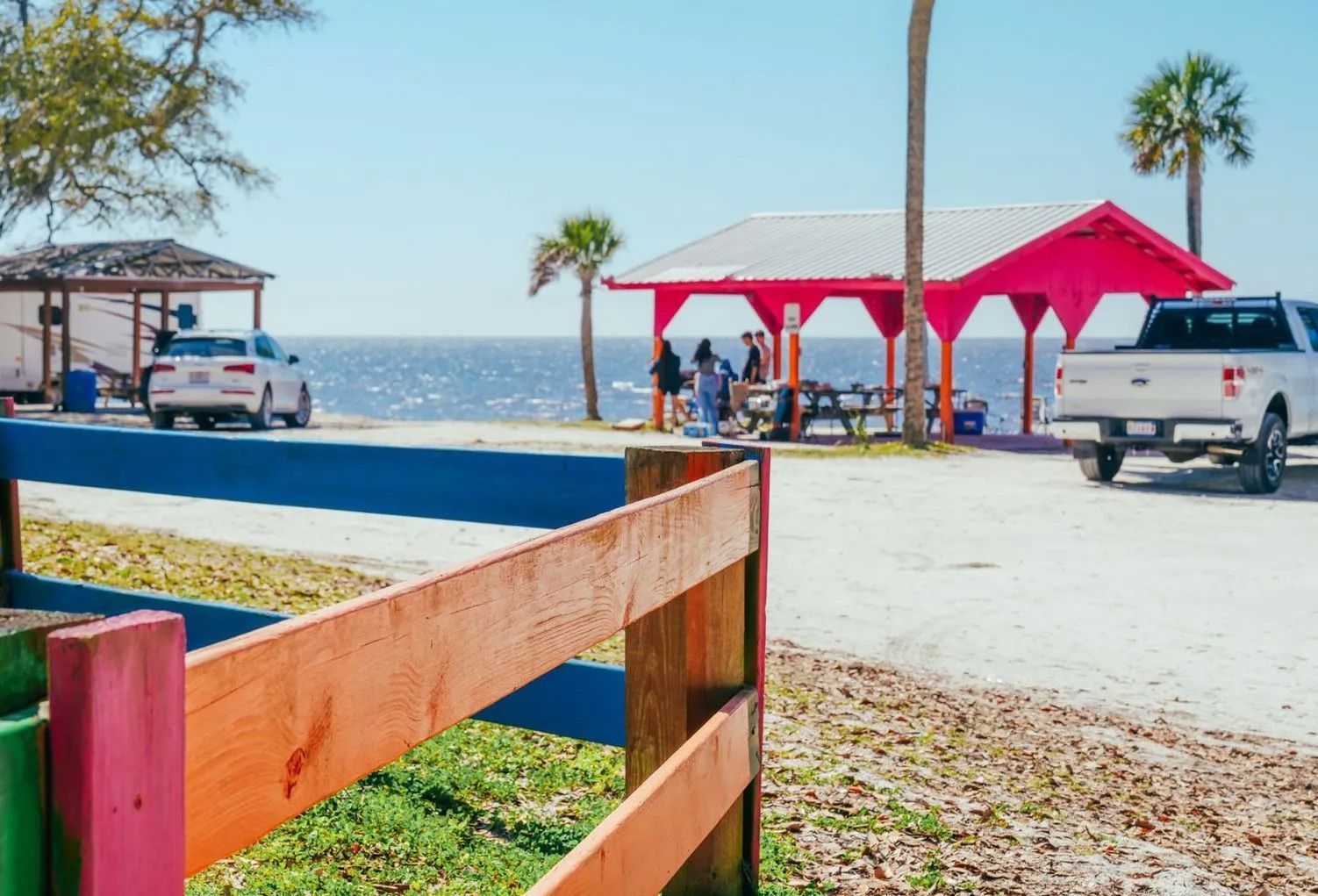 A white truck is parked in front of a picnic shelter on the beach.