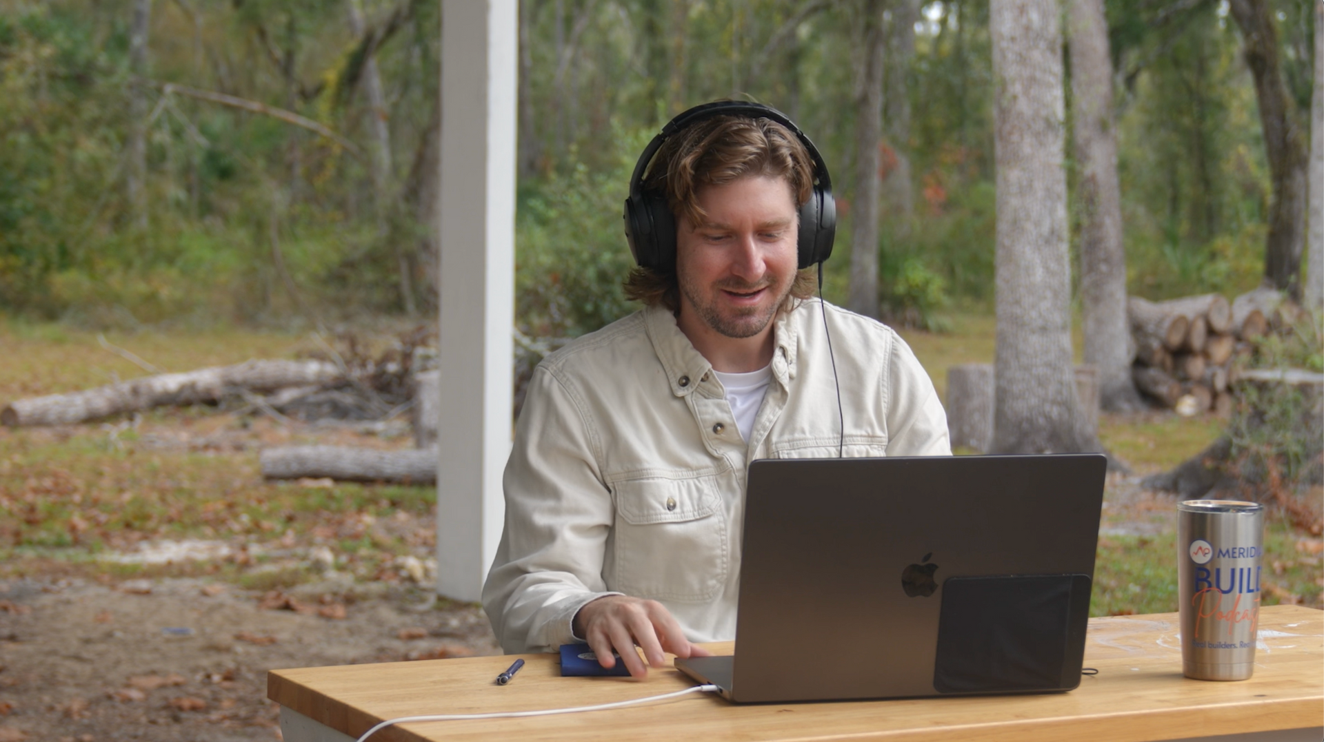 Man wearing headphones working on a laptop outside with a forest background.