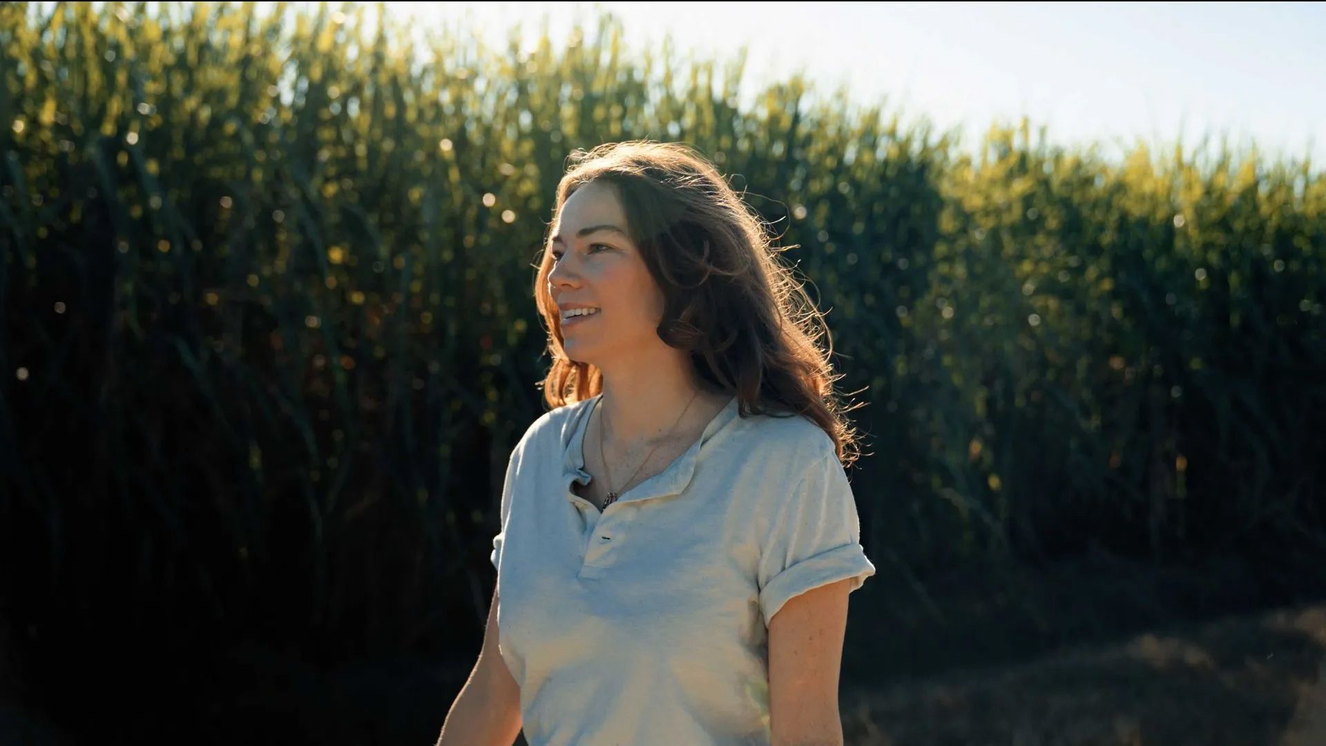 A woman in a white shirt is standing in a field of tall grass.