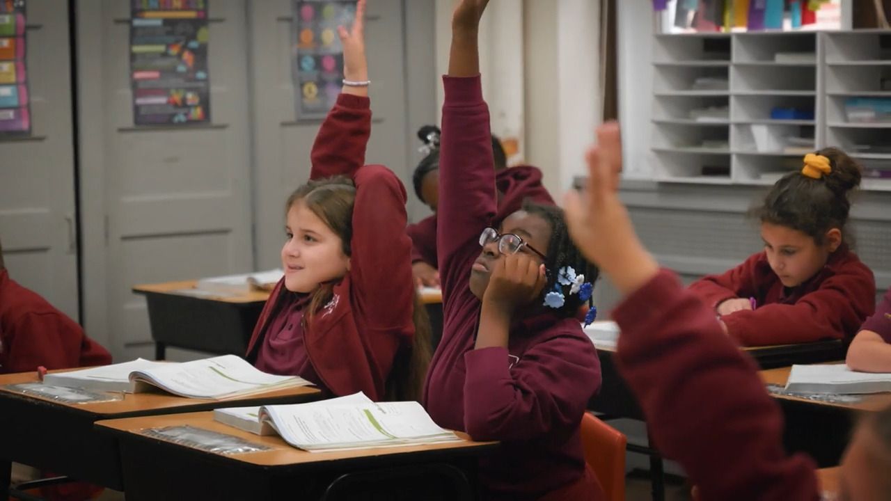 A group of children are raising their hands in a classroom.