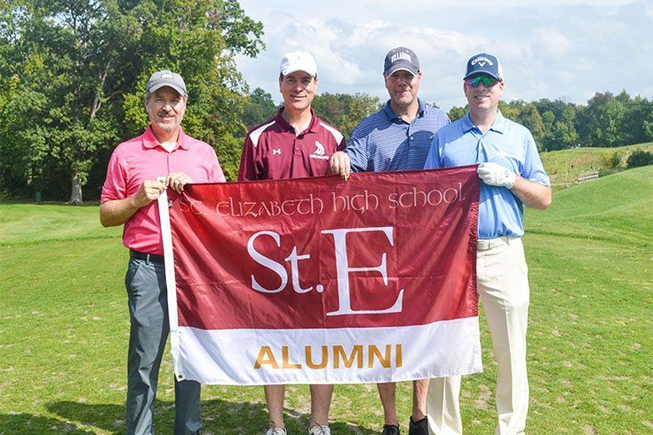 Four men holding a st. e alumni flag on a golf course