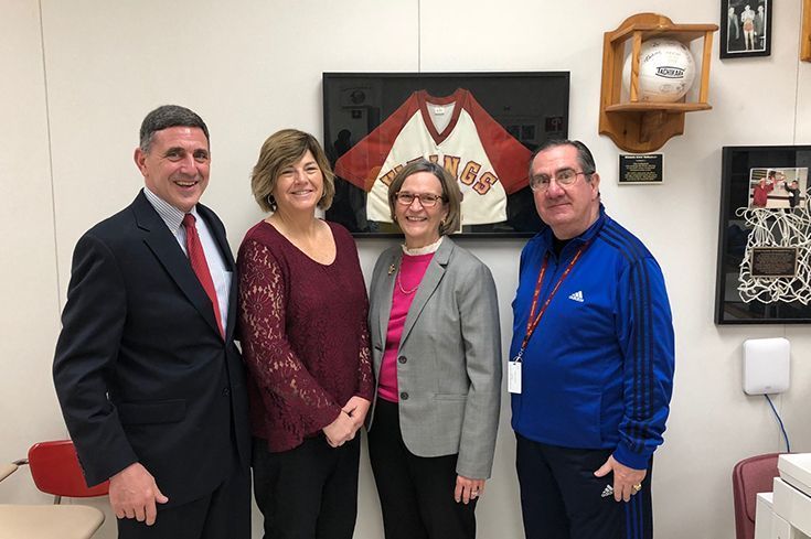 A group of people are posing for a picture in front of a framed basketball jersey.