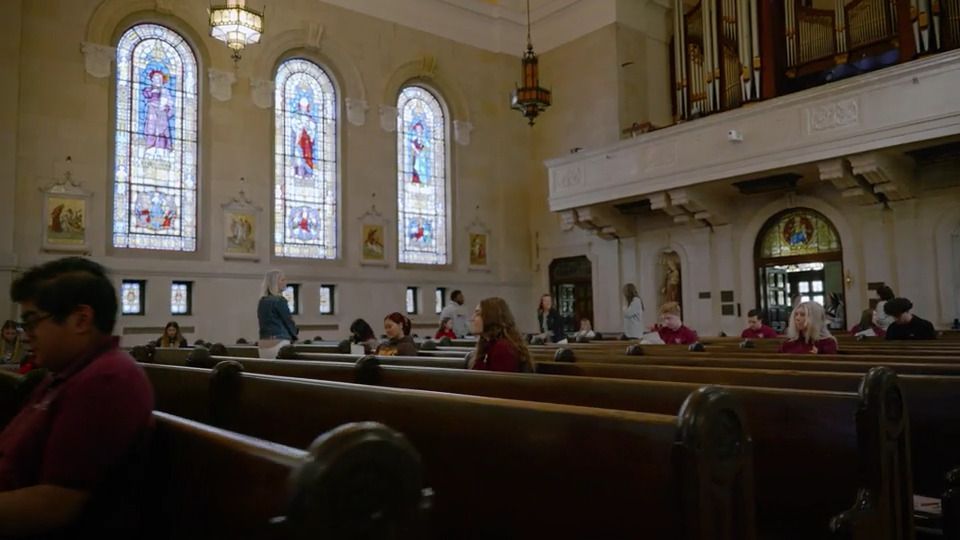 A group of people are sitting in a church with stained glass windows.