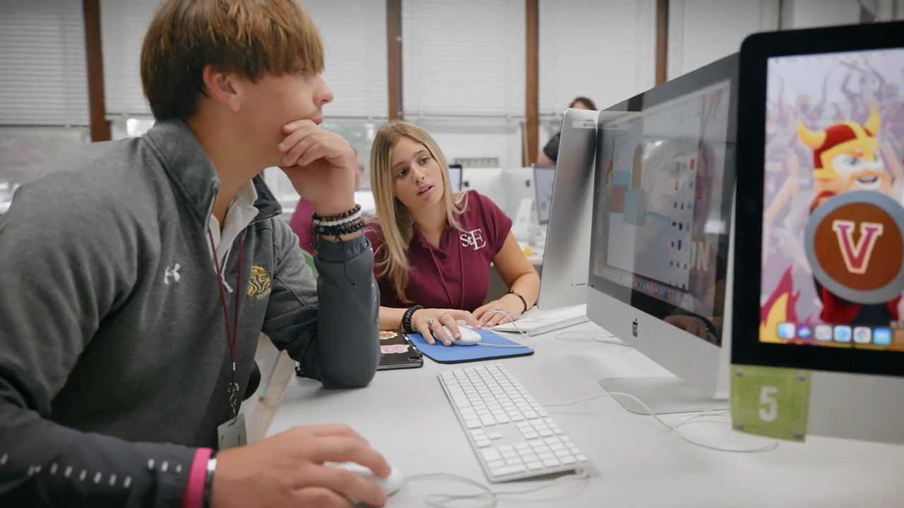 A man and a woman are sitting at a desk looking at a computer screen.