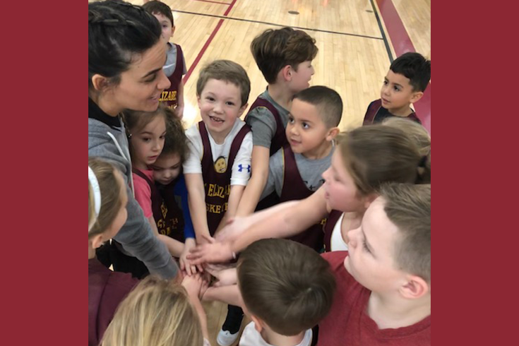 A group of children are huddled together on a basketball court.