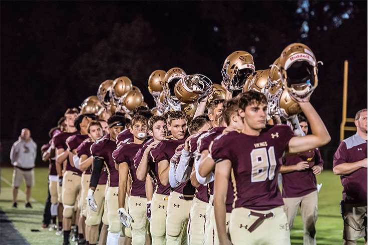 A football team is lined up on the field holding their helmets.