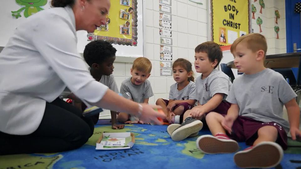 A teacher is reading a book to a group of children in a classroom.