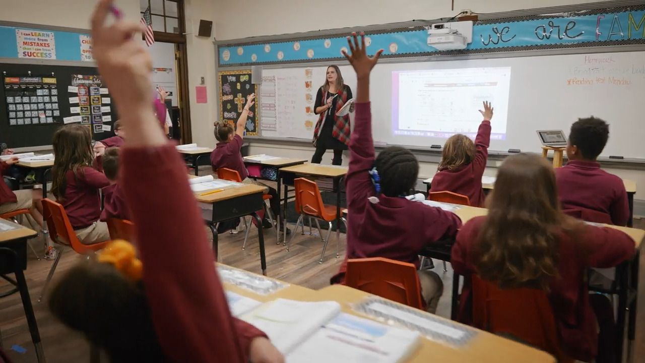 A group of children are raising their hands in a classroom.