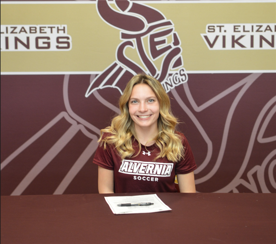 A woman is sitting at a table in front of a sign that says st. elizabeth vikings