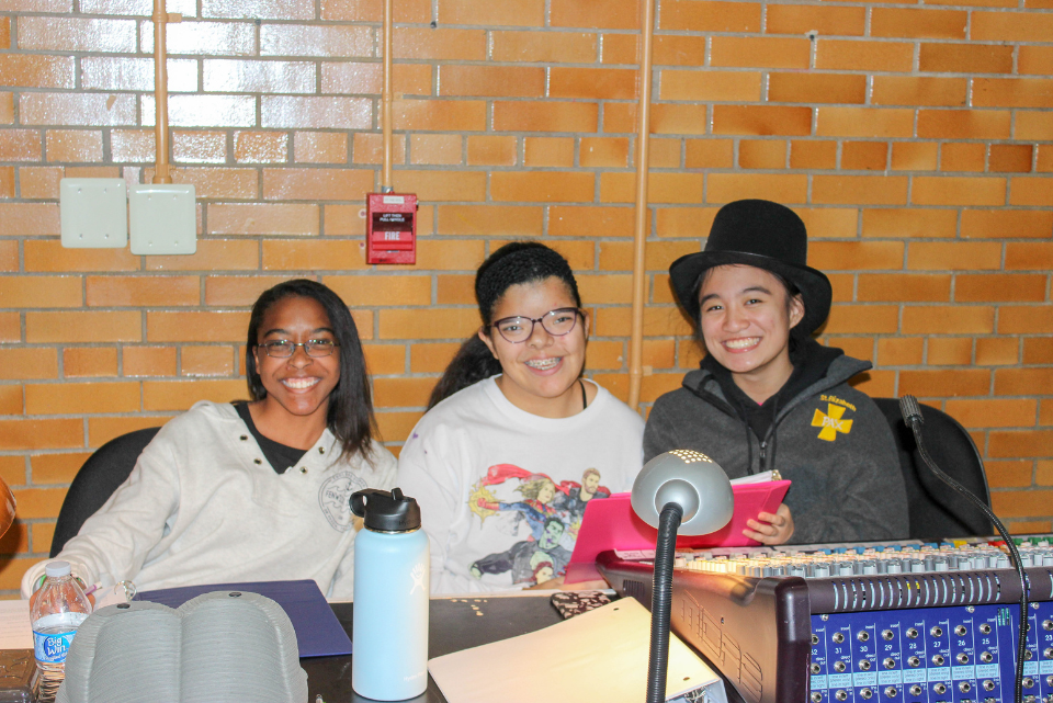 Three people are sitting at a table in front of a brick wall.