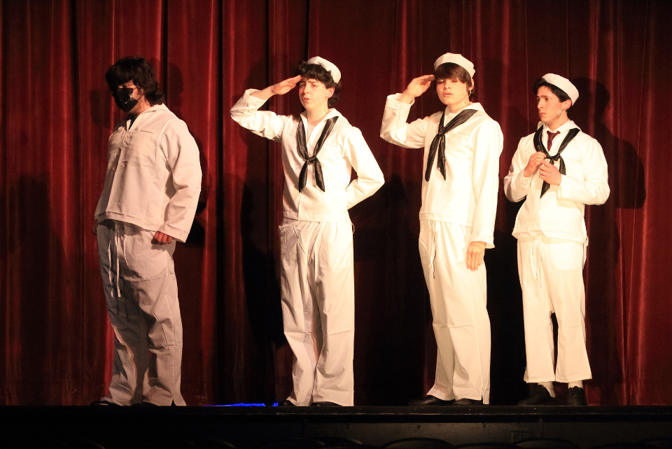 Four men in sailor uniforms salute on a stage