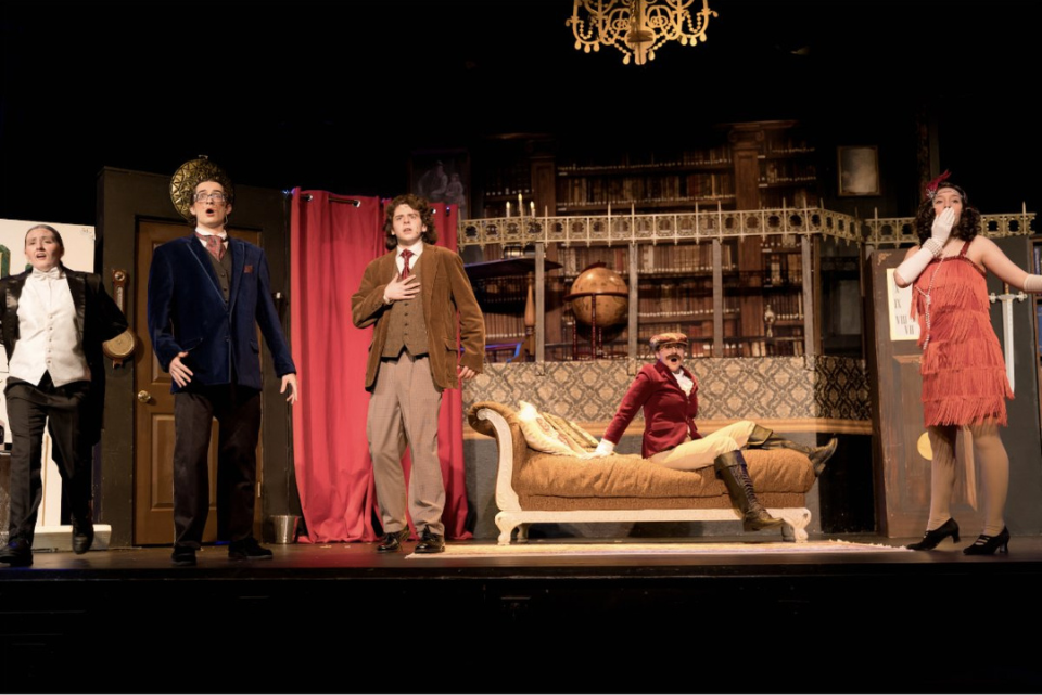 A group of people are standing on a stage in front of a couch.