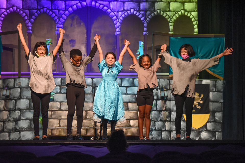 A group of children are standing on a stage with their arms in the air.
