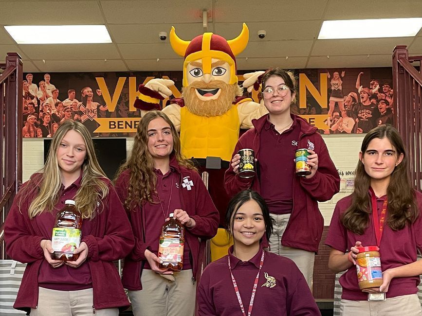 A group of girls are holding jars of peanut butter in front of a viking mascot.