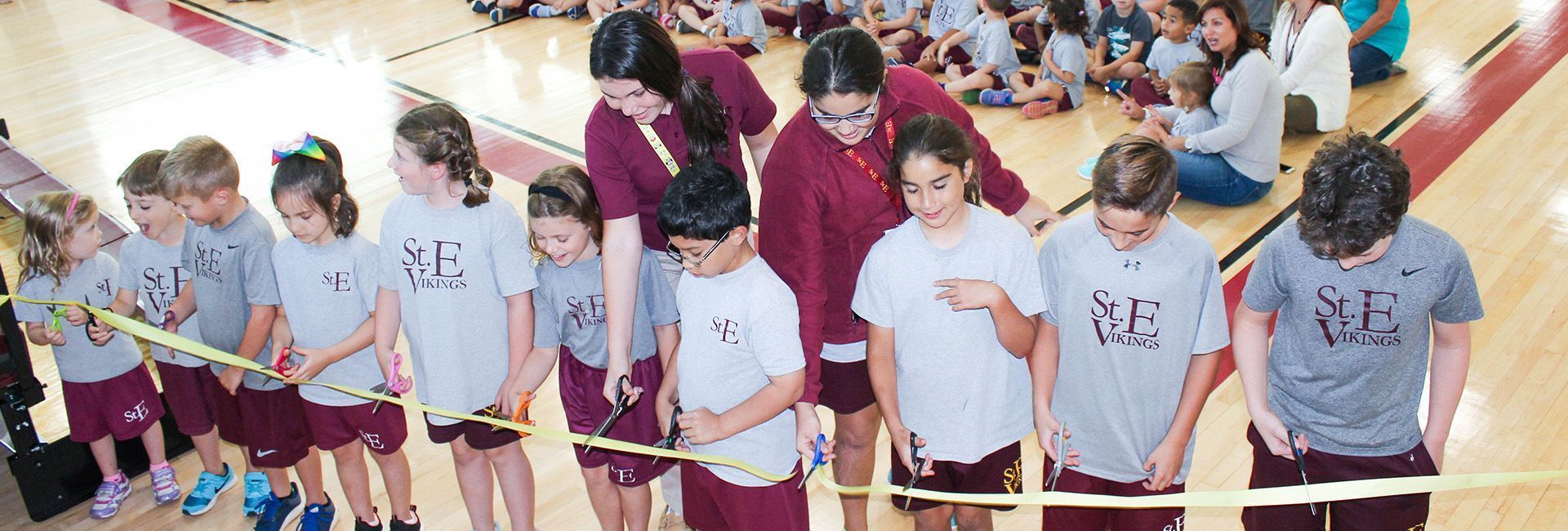 A group of children are standing on a basketball court holding a tape measure.