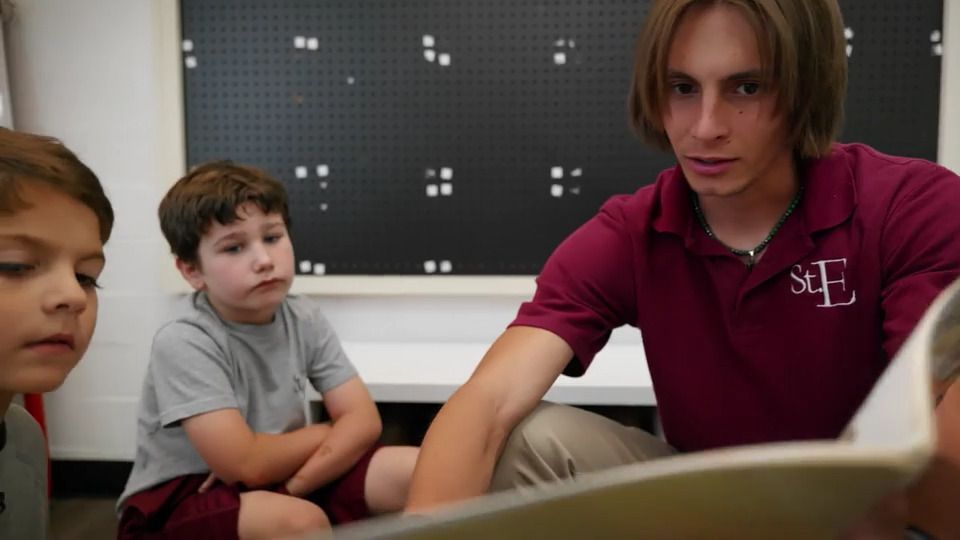 A man in a maroon shirt is reading a book to two young boys