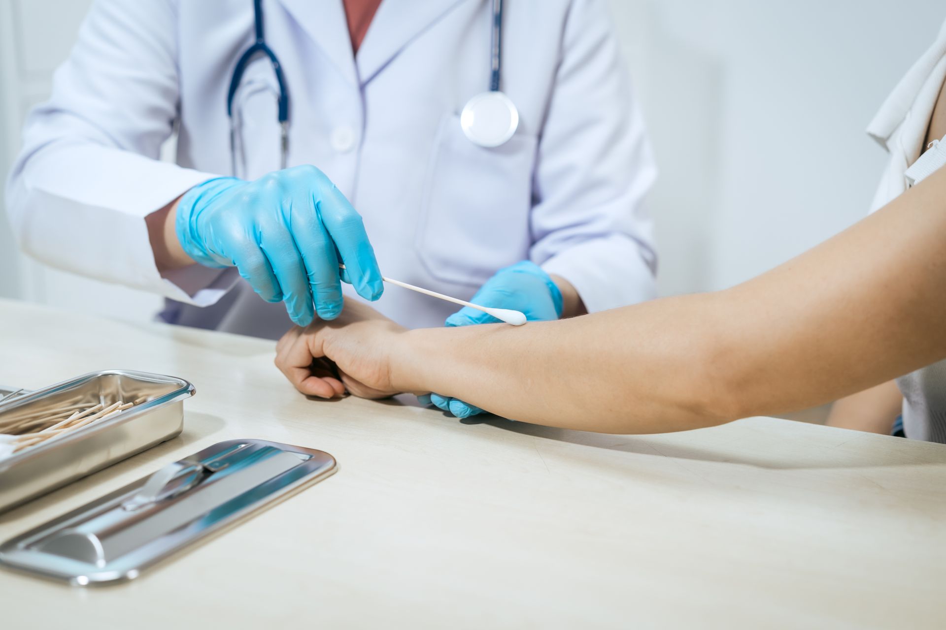 Healthcare provider cleans a minor arm wound with a cotton swab during a clinic visit.