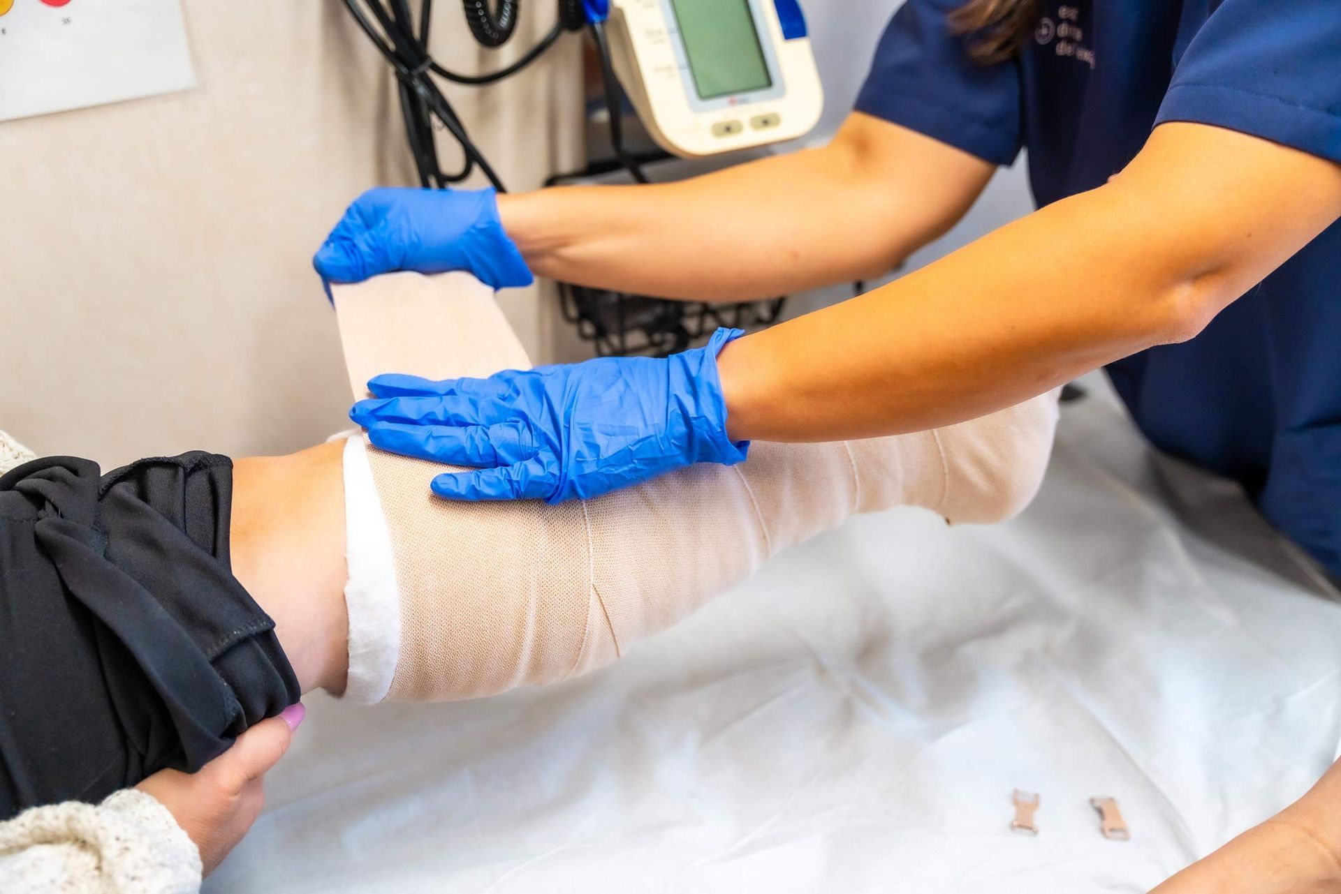 Clinician in gloves wrapping a bandage on a patient’s leg in a wound care clinic setting.