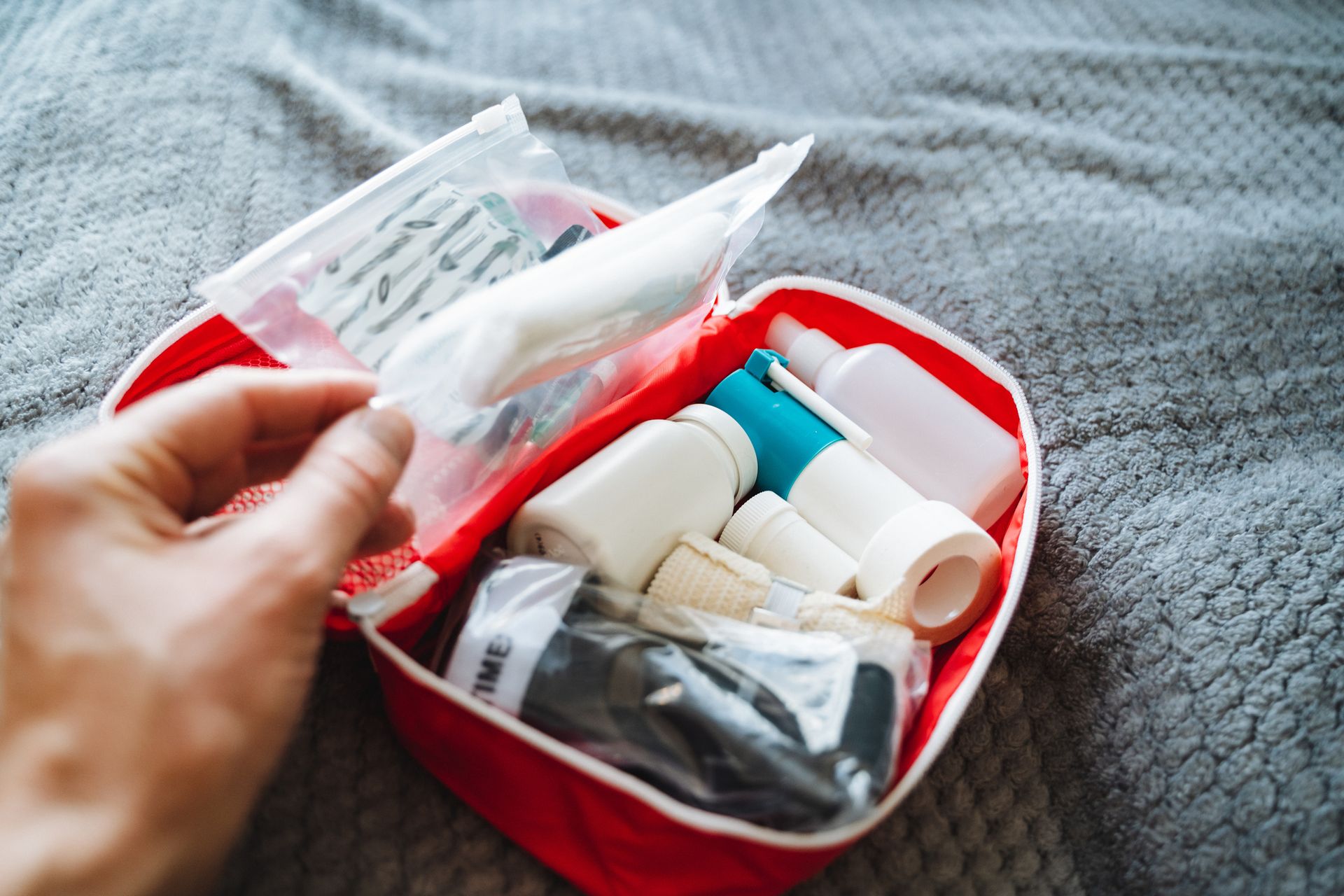 A person is slowly and carefully opening a first aid kit that is placed on a bed. A person is slowly and carefully opening a first aid kit that is placed on a bed.