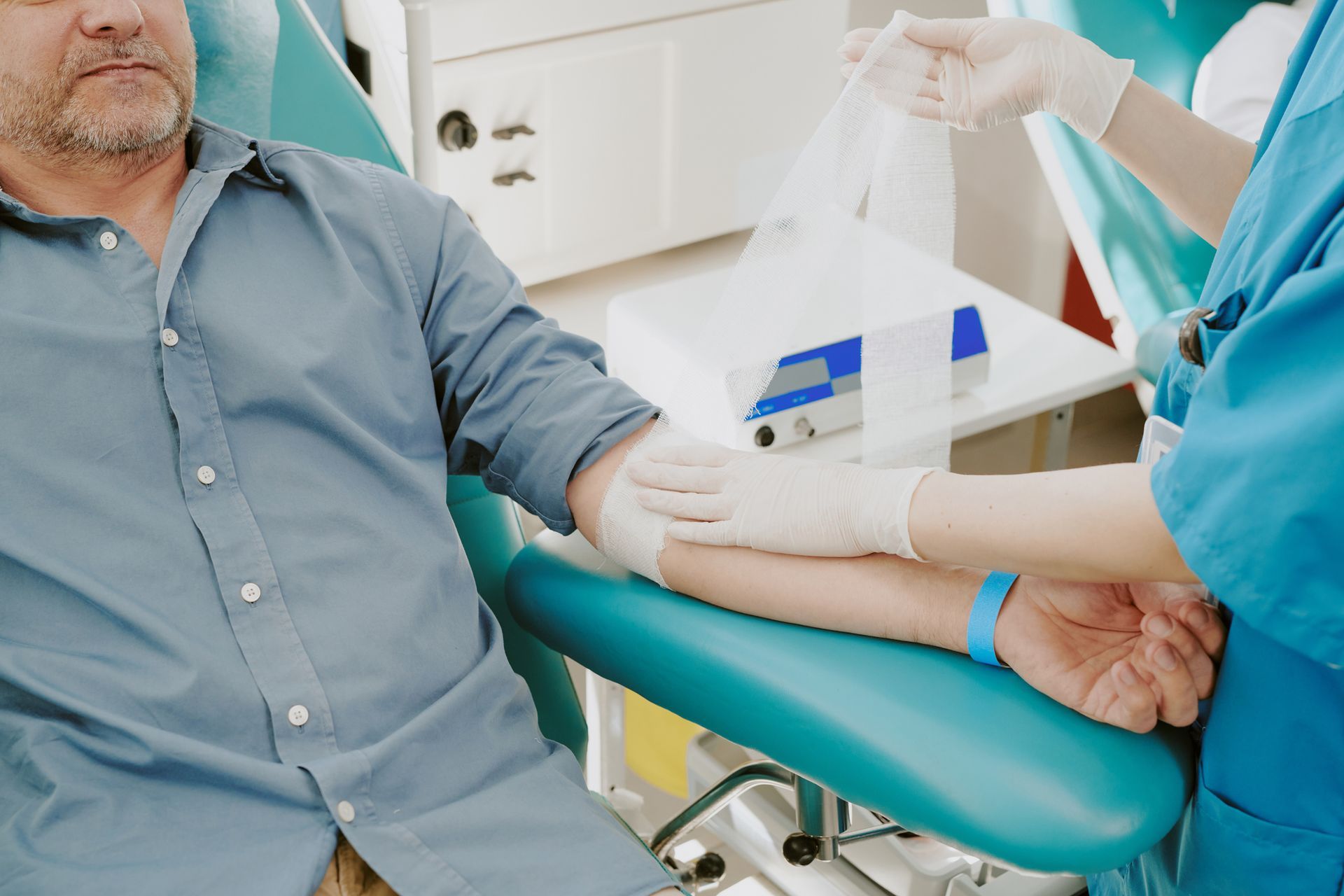 Man receiving medical care; nurse applying bandage to arm after blood draw, clinic setting.
