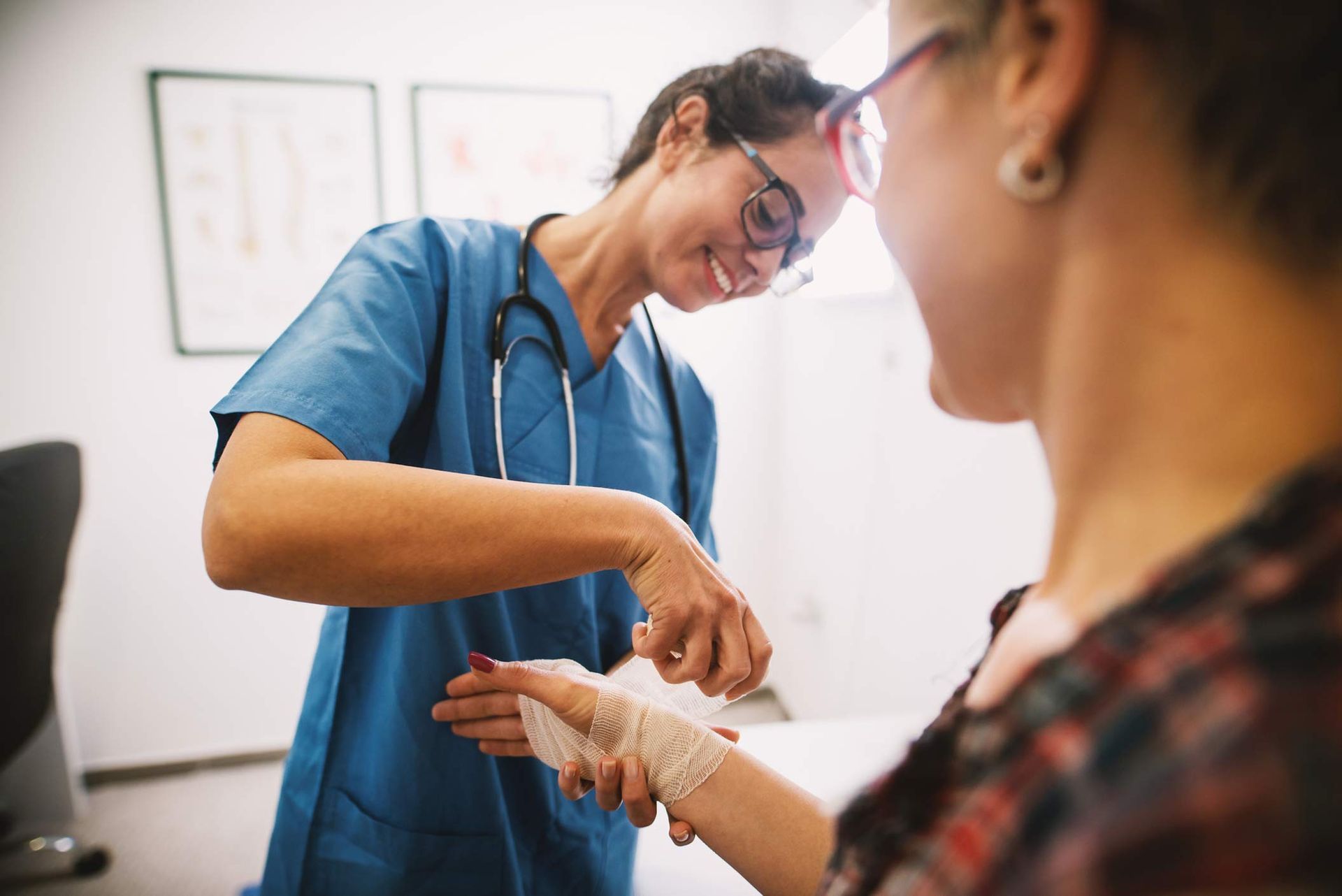 A nurse at the local medical clinic is bandaging a patient's hand with a medical bandage.