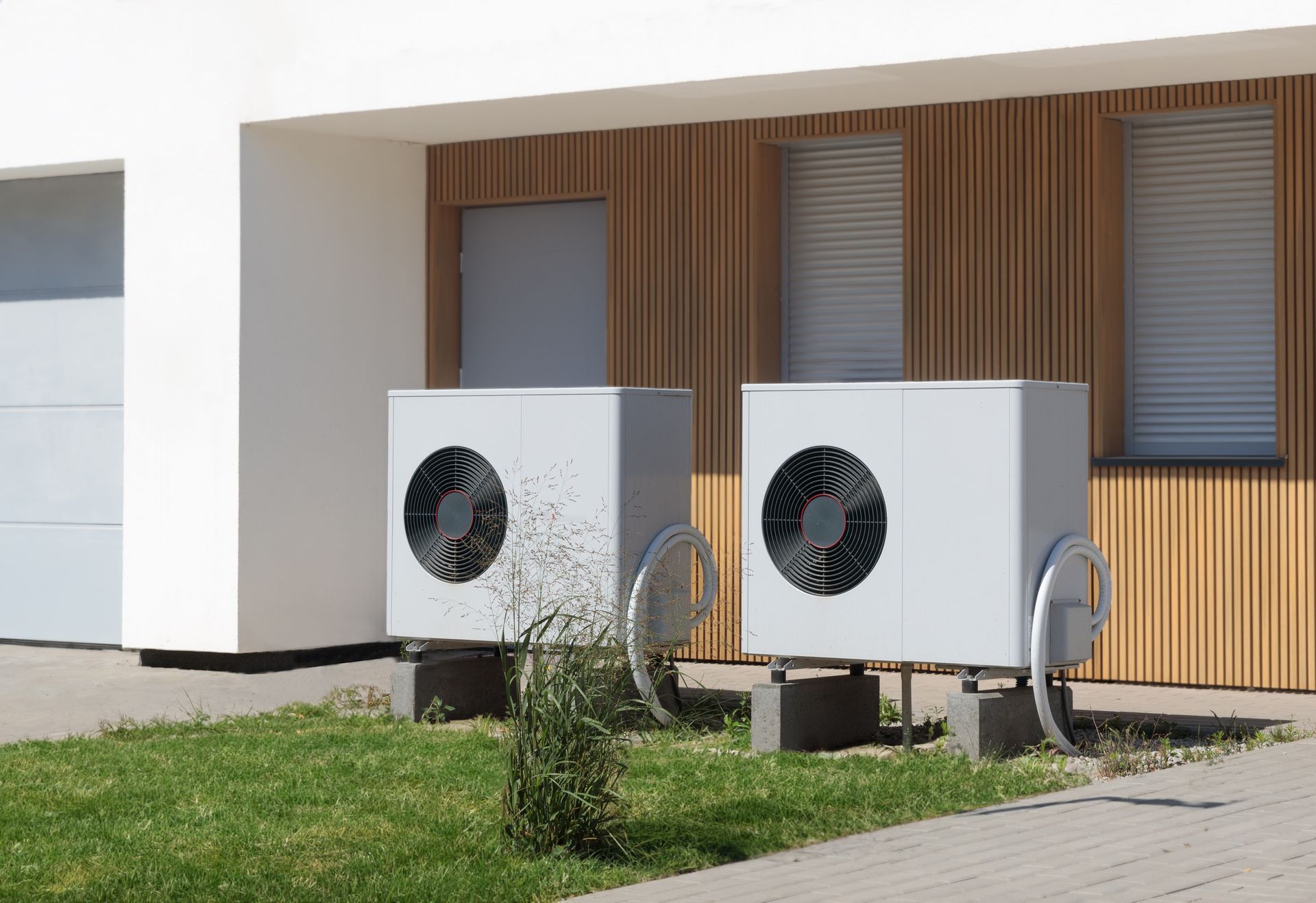 Two air conditioners are sitting in front of a house.
