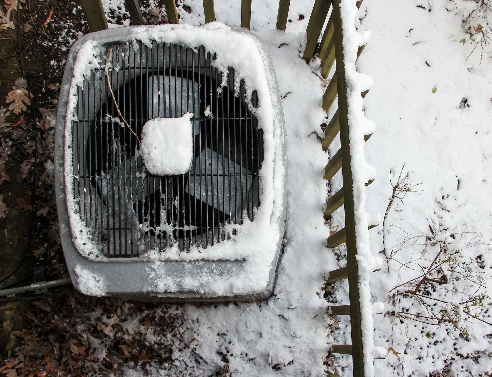 A fan is covered in snow next to a fence