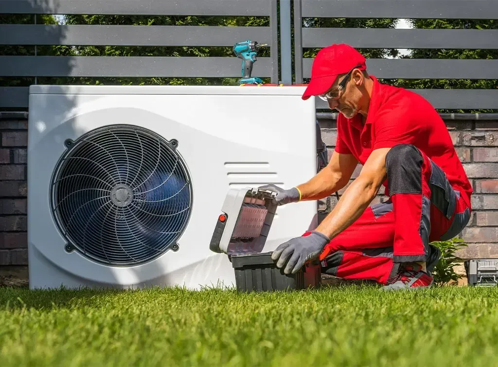 A man is working on an air conditioner in a backyard.