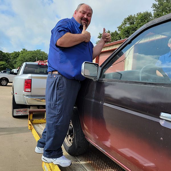 A man in a blue shirt is giving a thumbs up next to a car
