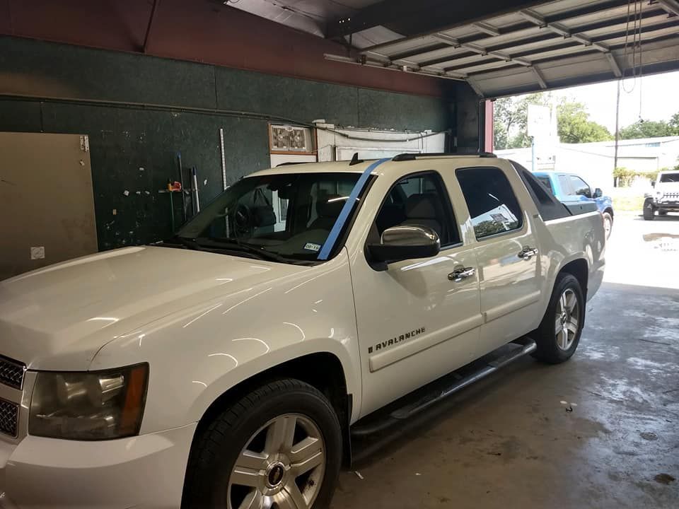 A white truck is parked in a garage with a blue tape covering the windshield.