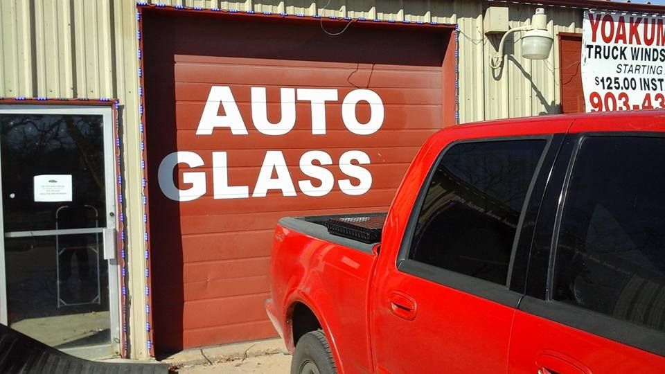 A red truck is parked in front of a building that says auto glass