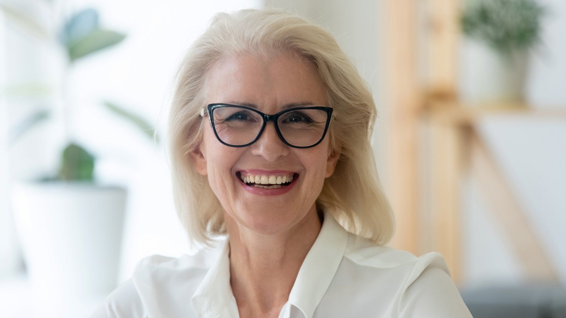 A woman wearing glasses and a white shirt is smiling.