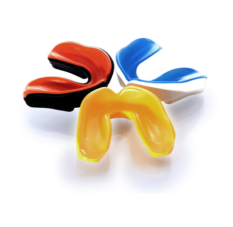 Three mouth guards of different colors are sitting on a white surface