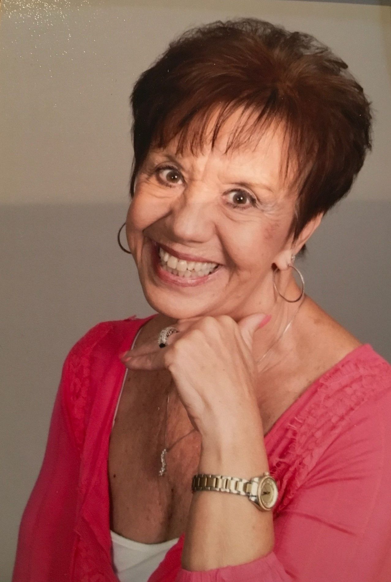 A woman wearing a pink shirt and a watch is smiling for the camera.