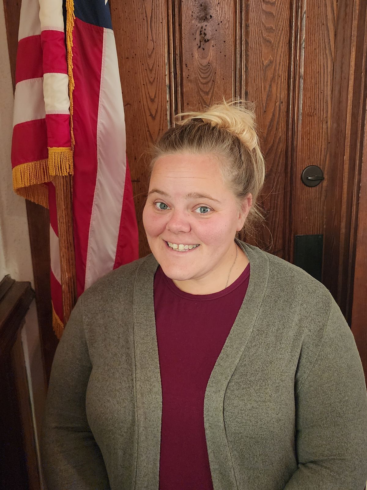 A woman is smiling in front of an american flag