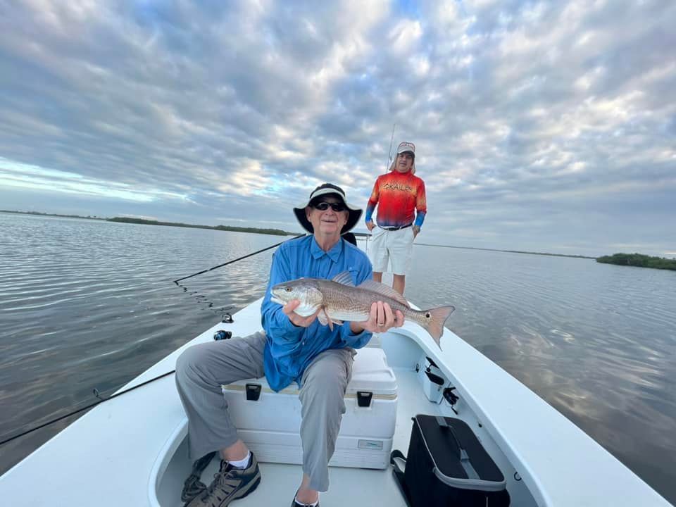 Man holding a redfish on a boat, another person in background, cloudy sky.