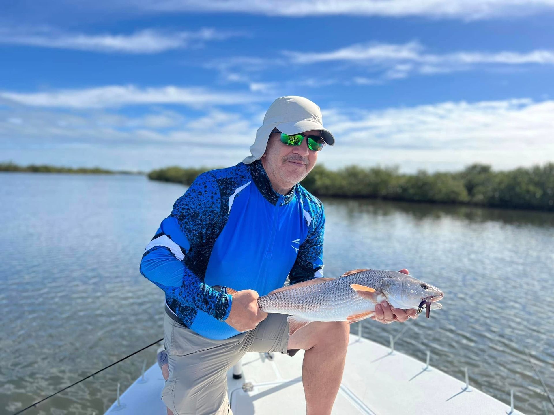 Man holding a redfish on a boat under a sunny blue sky.