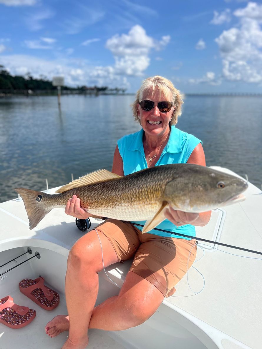 Woman on boat holds a large fish, smiling. Blue water and sky in the background.