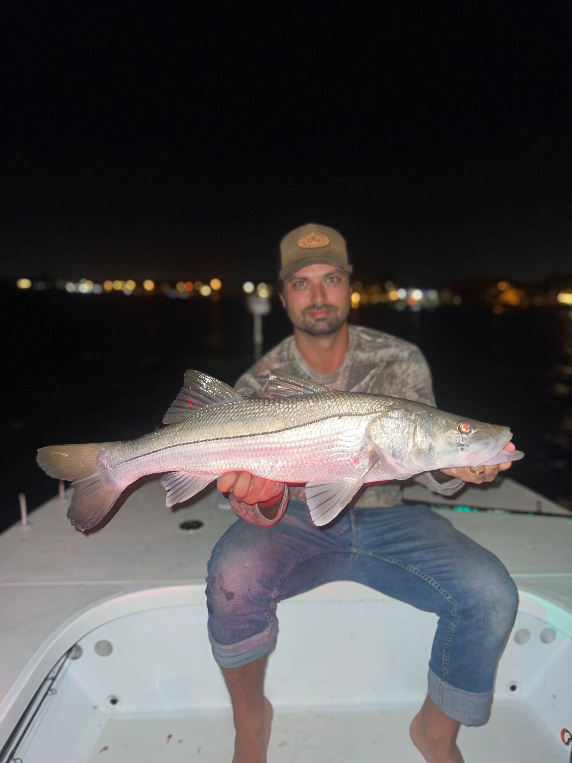 Man holding a large fish on a boat at night.