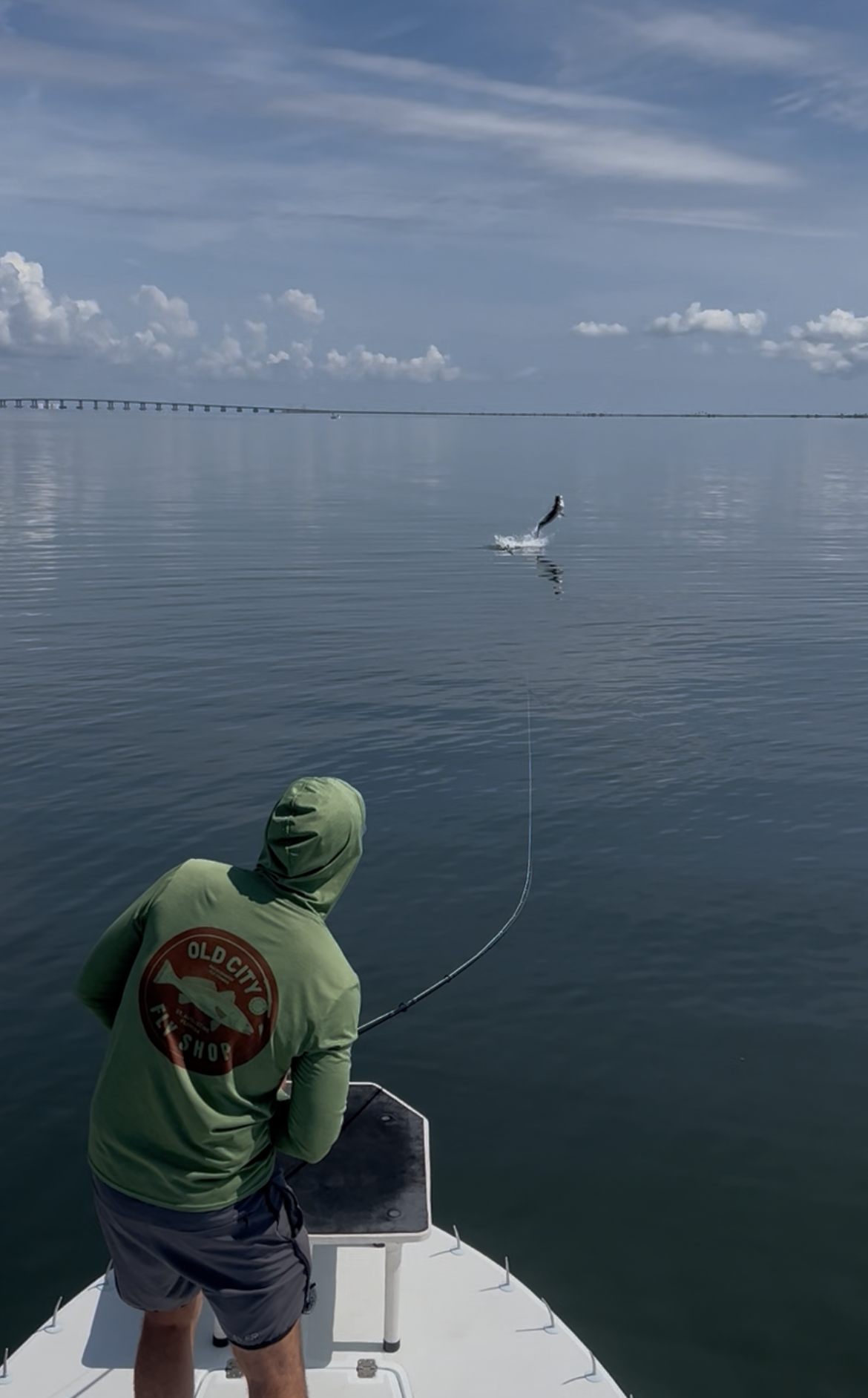 Man on a boat holding a red drum fish. He's wearing a hat and jacket with a river background.