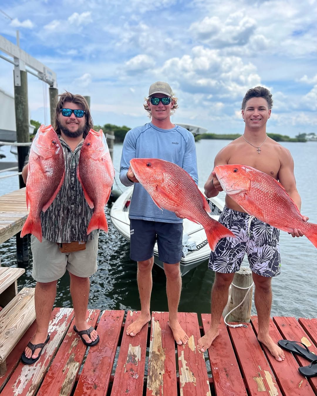 Man holding a large, black crappie fish, standing in front of trees, wearing a hat, sunglasses, and a white shirt.