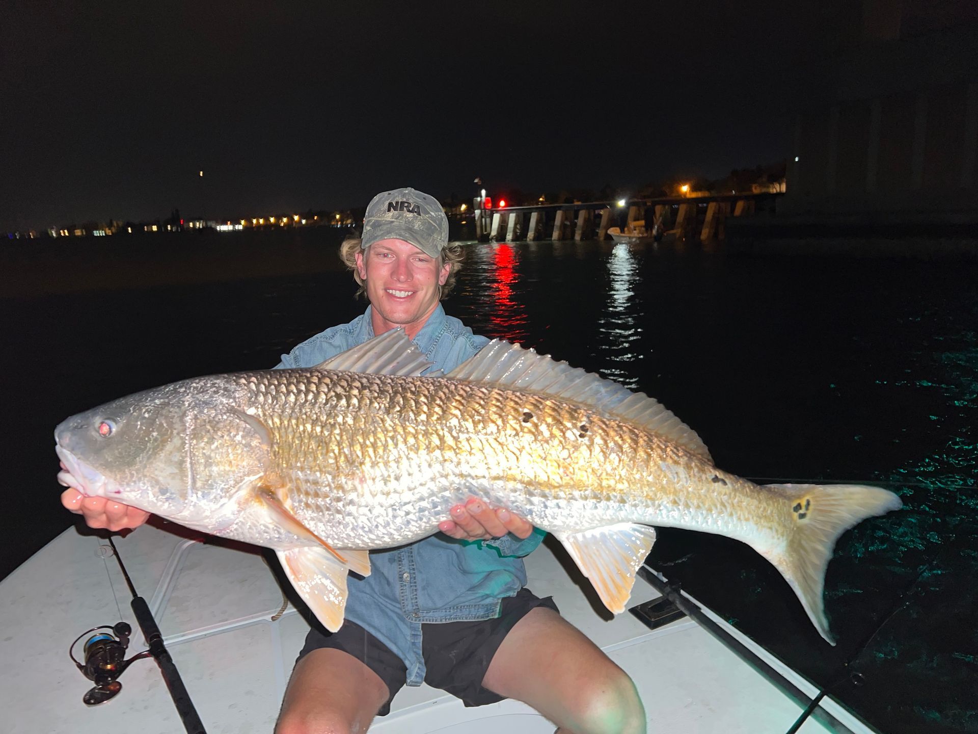 Man smiles holding a large, reddish-brown fish on a boat, ocean backdrop, overcast sky.