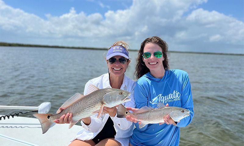 Boat floats on calm water reflecting a cloudy sky and bordering lush green trees.