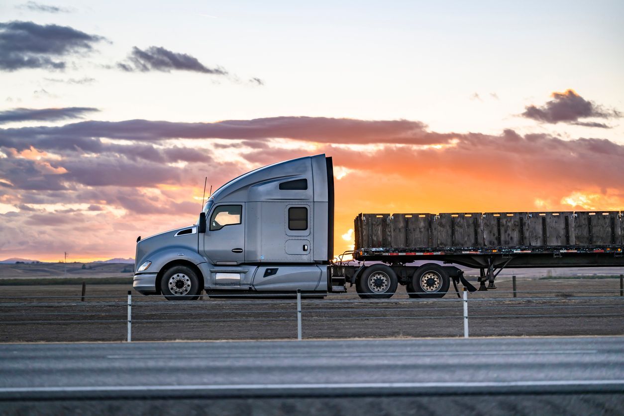 A semi truck is driving down a highway at sunset.