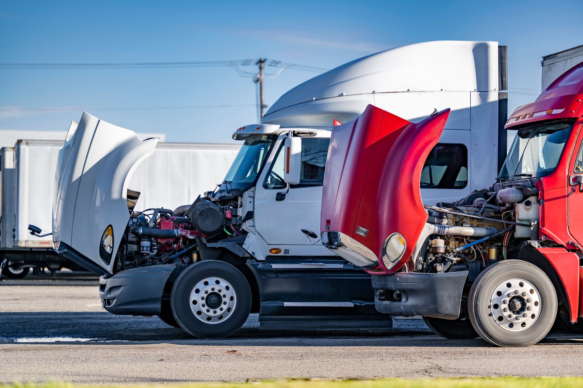 Two semi trucks are parked next to each other with their hoods open.