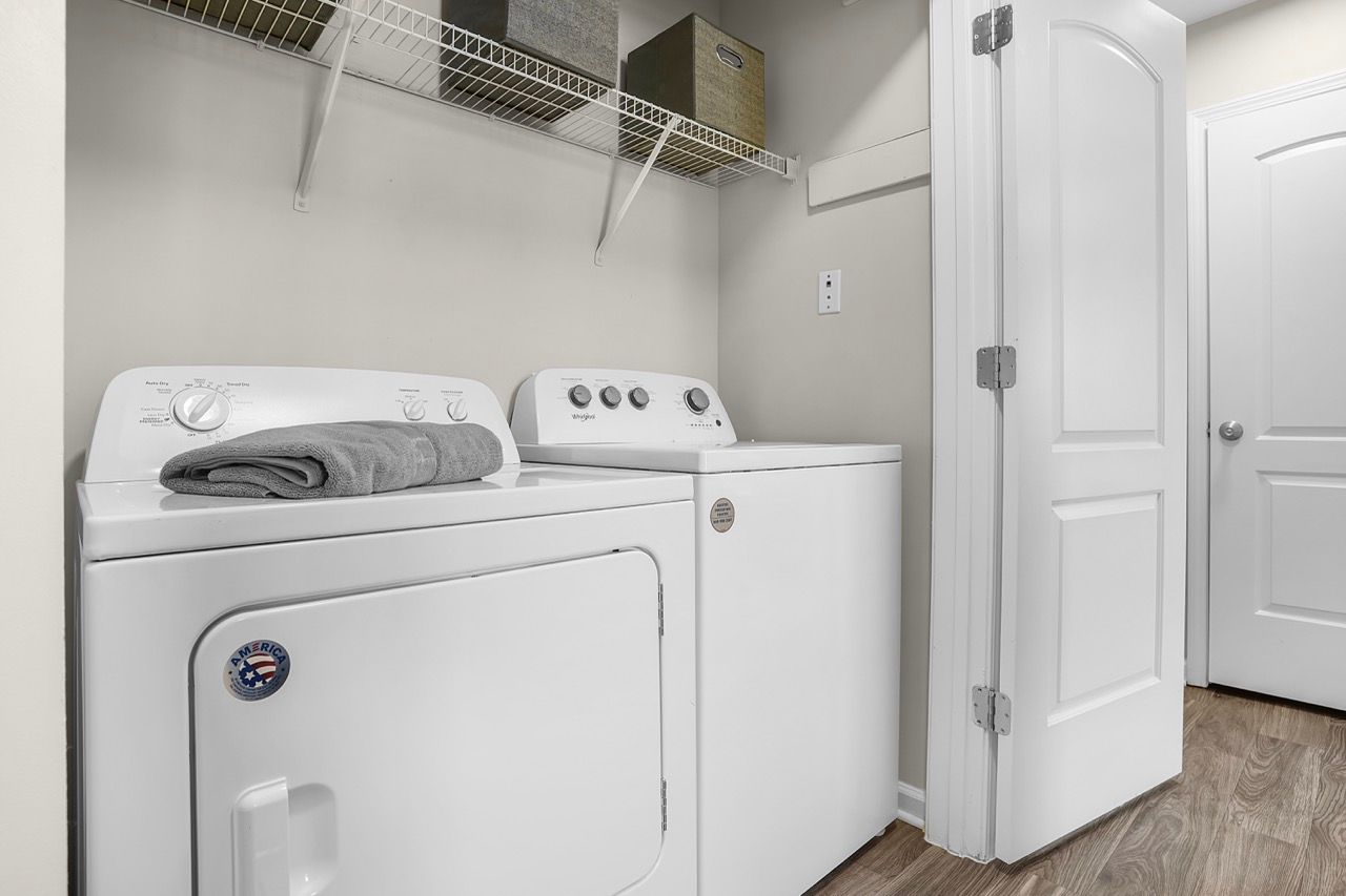 White washer and dryer in a compact laundry closet with a wire shelf and storage bins.