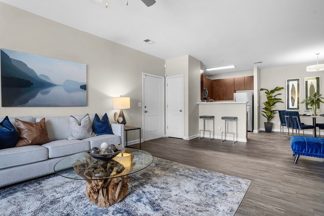 Open-concept living area with gray sofa, glass coffee table, and kitchen in the background.