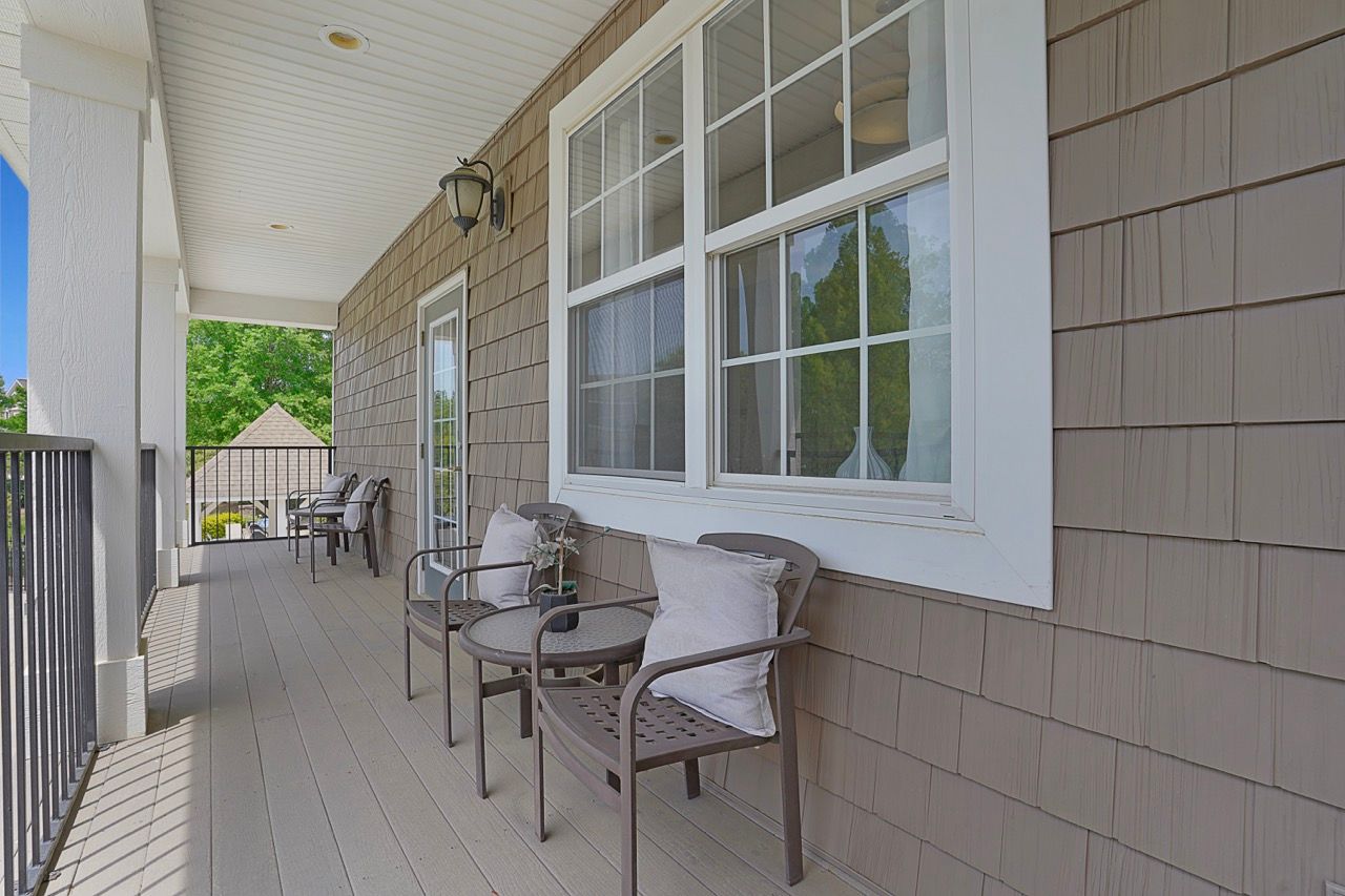 Outdoor apartment balcony with metal chairs and cushions along a shingled wall.